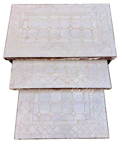 Three rectangular nesting tables stacked vertically, featuring a white mother-of-pearl inlay with a geometric pattern and gold-toned accents, set against a plain white background.