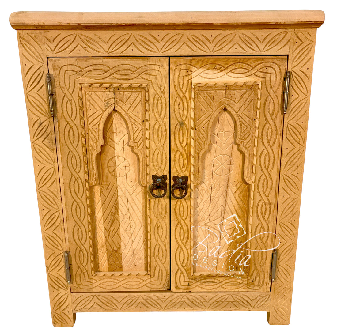 A light natural wood cabinet with intricate hand-carved geometric patterns and arched door panels, featuring dark metal ring pulls, set against a plain white background.