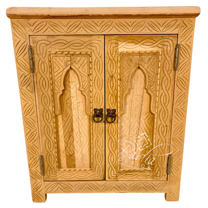 A light natural wood cabinet with intricate hand-carved geometric patterns and arched door panels, featuring dark metal ring pulls, set against a plain white background.