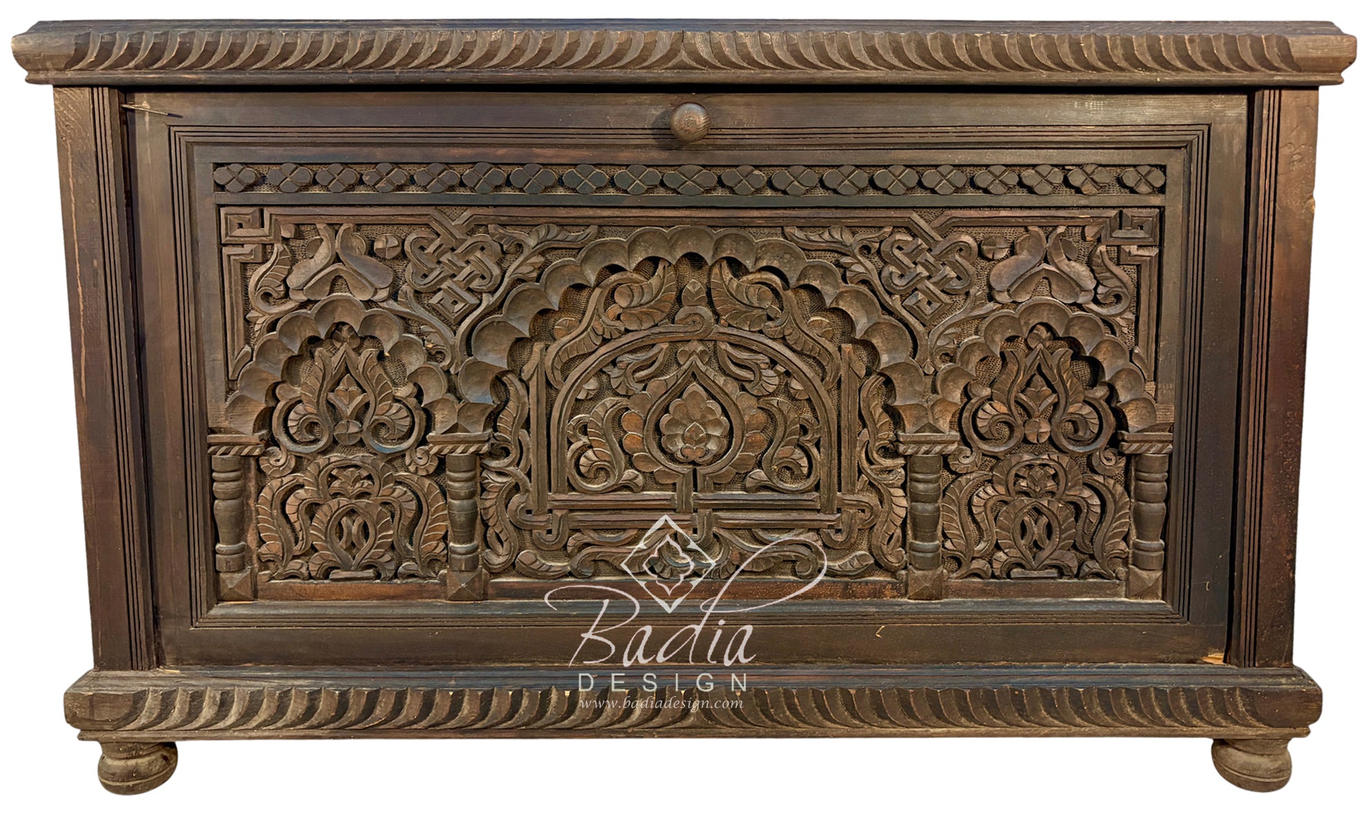 An ornate dark brown carved wooden chest or cabinet with intricate floral and arch motifs, shown against a plain white background. A &