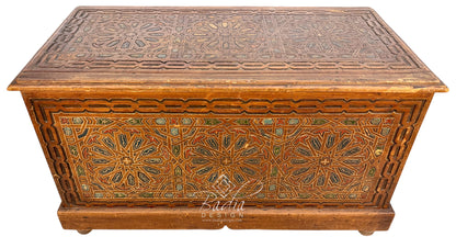 An ornate rectangular wooden storage chest or trunk with carved geometric and floral patterns, featuring a warm brown finish and decorative inlays, shown against a plain white background.