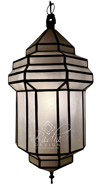A hanging lantern-style pendant light with a black metal frame and translucent warm-toned panels, shown against a plain white background. A watermark reading &